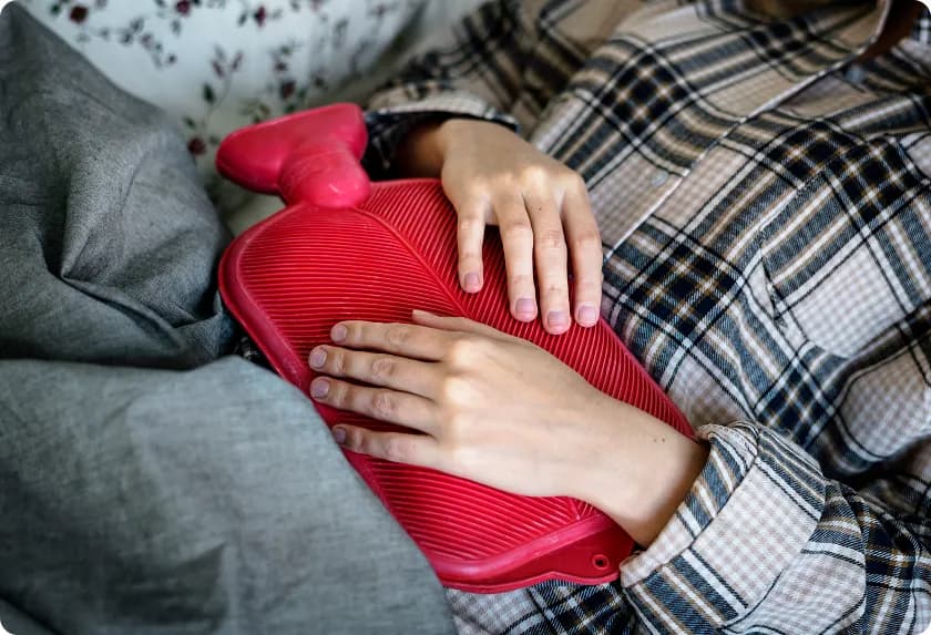 Person applying a red heating pad for constipation to ease stomach pain