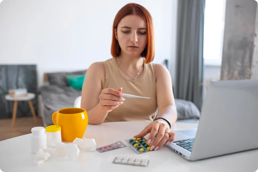 A woman taking medication while tracking her health on a laptop, highlighting the importance of managing lupus symptoms, including lupus nephritis stages and skin disease.
