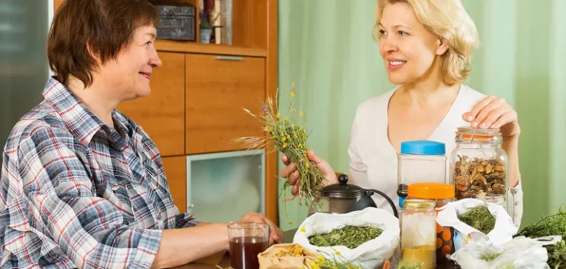 Two women discussing herbal teas and natural remedies for constipation at a table.