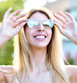 Smiling woman adjusts shades showing how sunglasses protect from uv rays