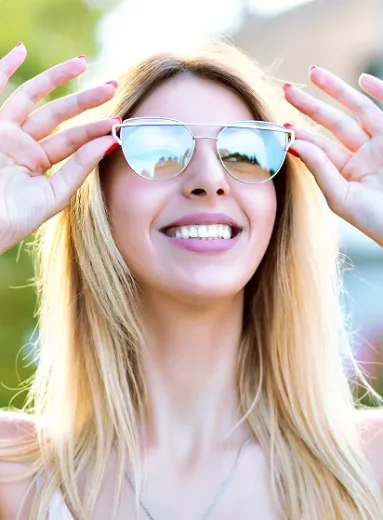 Smiling woman adjusts shades showing how sunglasses protect from uv rays