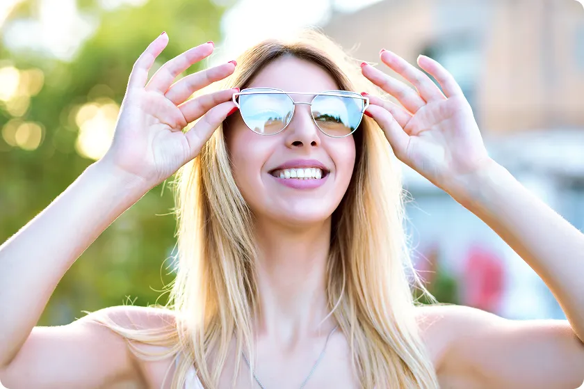 Smiling woman adjusts shades showing how sunglasses protect from uv rays