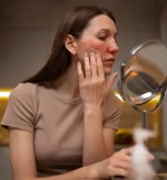 A woman looks in the mirror assessing a facial butterfly rash related to lupus life expectancy.