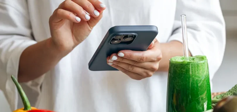 Person holding a smartphone near healthy food during a social media detox.