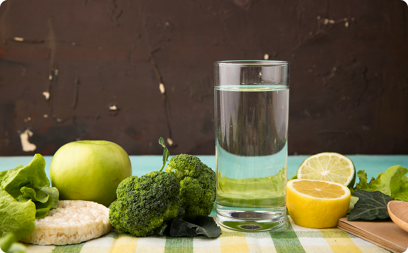 Glass of water beside apples and broccoli—common foods that relieve constipation.