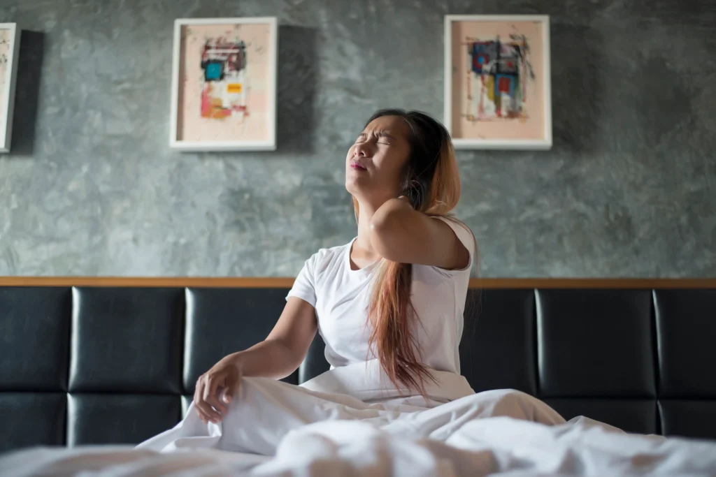 A woman waking up in bed with an expression of intense joint pain at night.