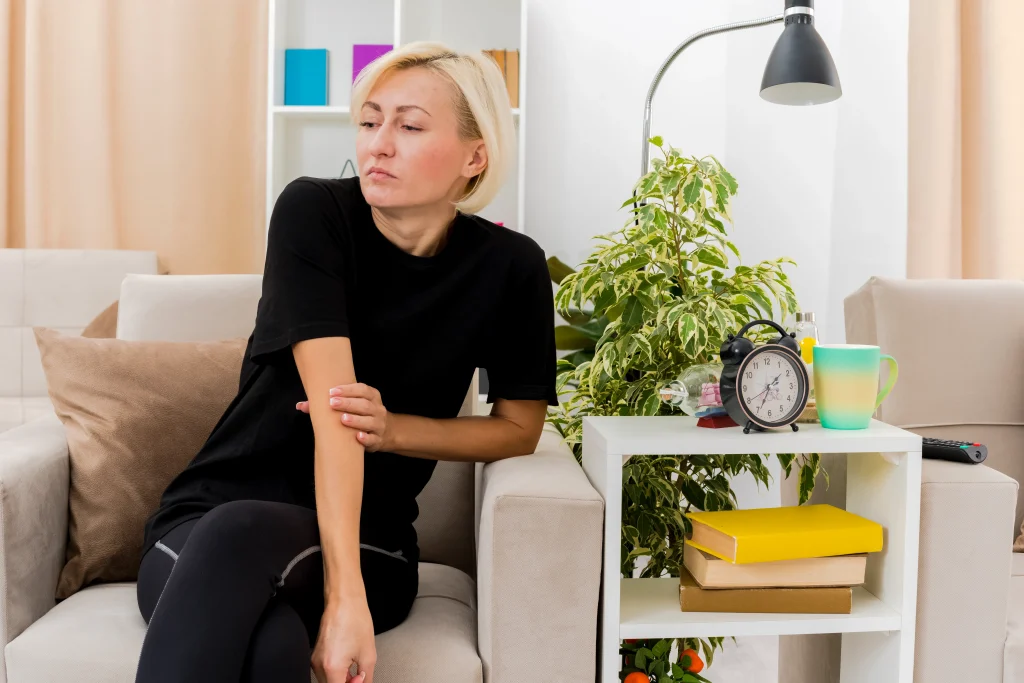 A woman sitting on a couch touching her sore arm reflecting on why does pain get worse at night.
