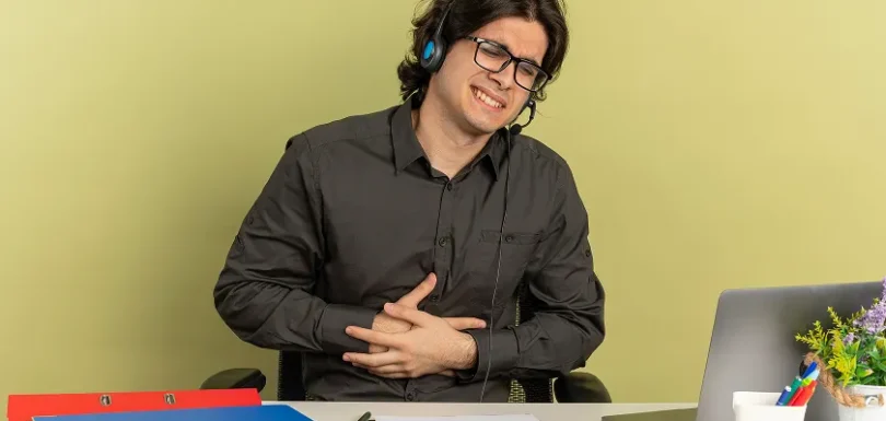 Remote worker grimacing from nausea and gerd beside laptop
