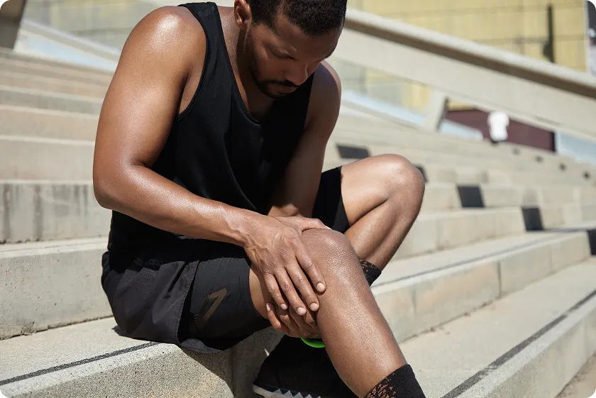 Man sitting on steps holding his knee, showing lupus symptoms men experience.