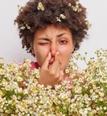 A woman with grass pollen allergy symptoms touching her irritated nose outdoors