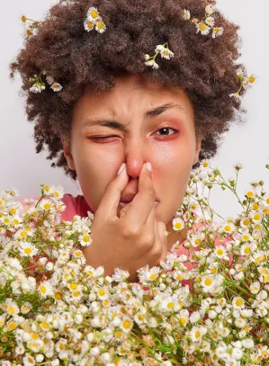 A woman with grass pollen allergy symptoms touching her irritated nose outdoors