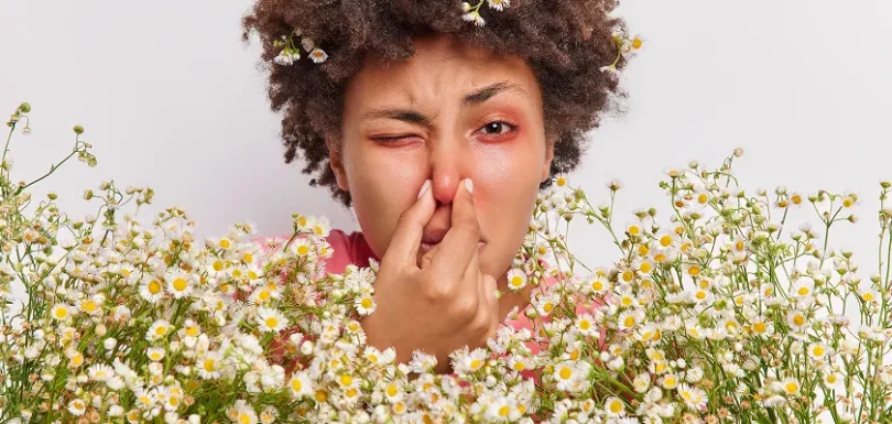 A woman with grass pollen allergy symptoms touching her irritated nose outdoors