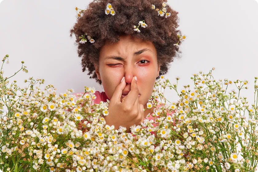 A woman with grass pollen allergy symptoms touching her irritated nose outdoors