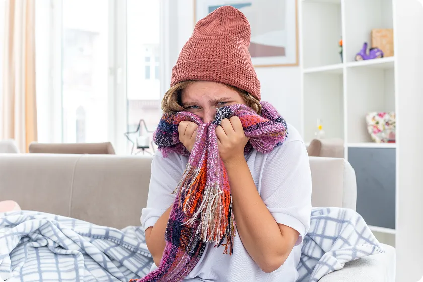 Person bundled in scarf experiencing winter allergies symptoms at home.