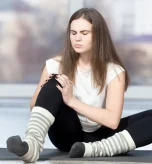 Young woman holding sore knee from diabetics legs discomfort