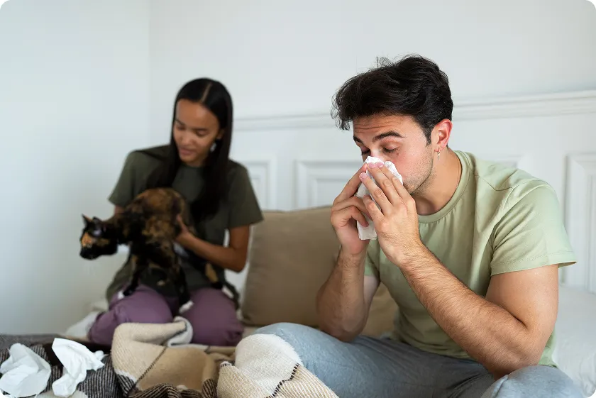 Man sneezing near cat showing allergic reaction to dog dander indoors