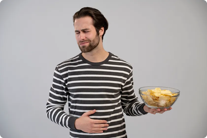 Man experiencing stomach discomfort holding a bowl of chips to highlight foods to avoid diverticulosis.