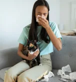 Woman holding cat experiencing symptoms for cat allergy treatment at home