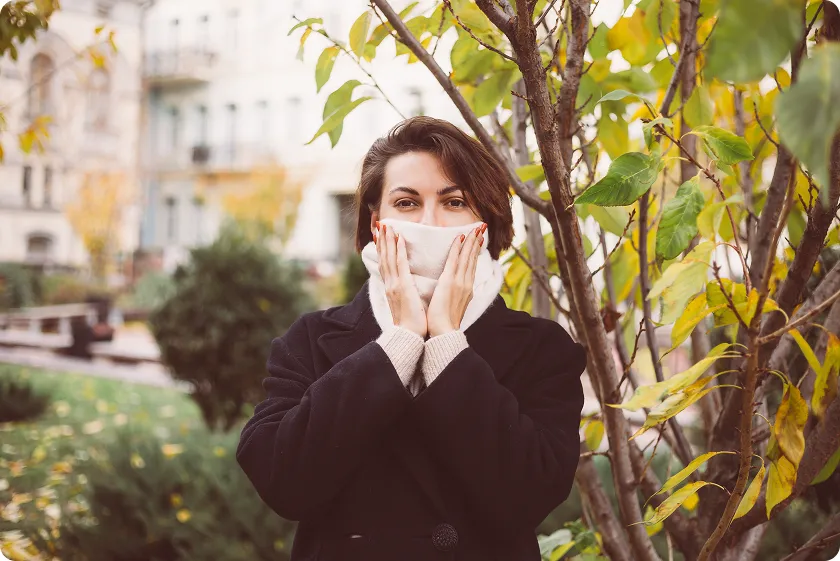 A woman near trees is protecting her face from pollen allergy rash triggers