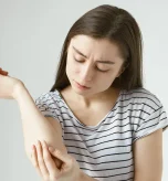 Woman scratching arm due to allergic reaction to wasp sting, yellow jacket allergy possible.