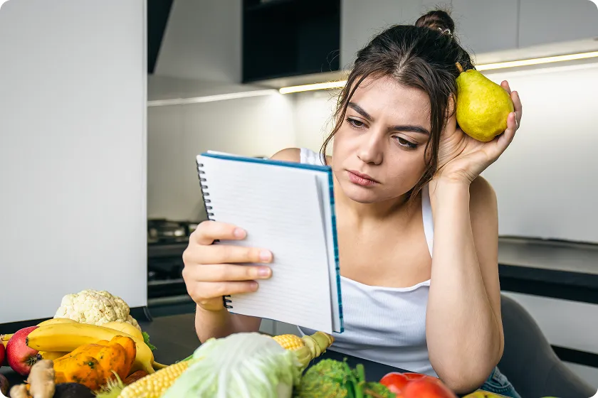 Confused woman reviewing a meal plan with fresh fruits and foods to prevent diverticulitis.