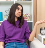 Confused woman sitting next to a clock tracking irregular periods during perimenopause.