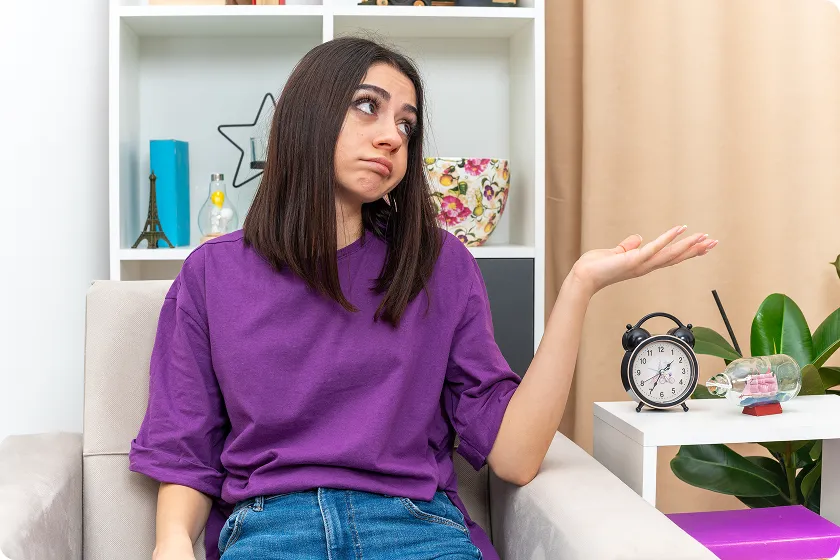 Confused woman sitting next to a clock tracking irregular periods during perimenopause.