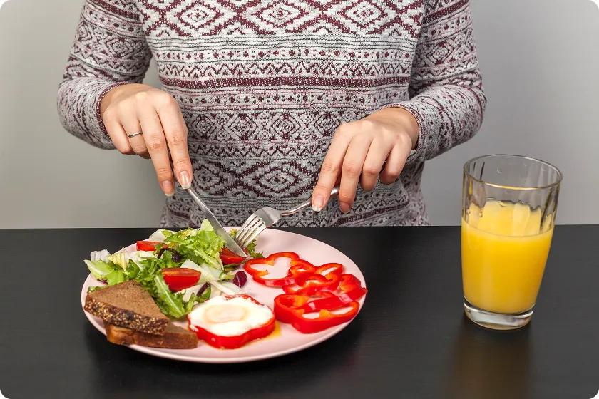 Person eating a healthy breakfast with salad and eggs following a diverticulitis diet plan.