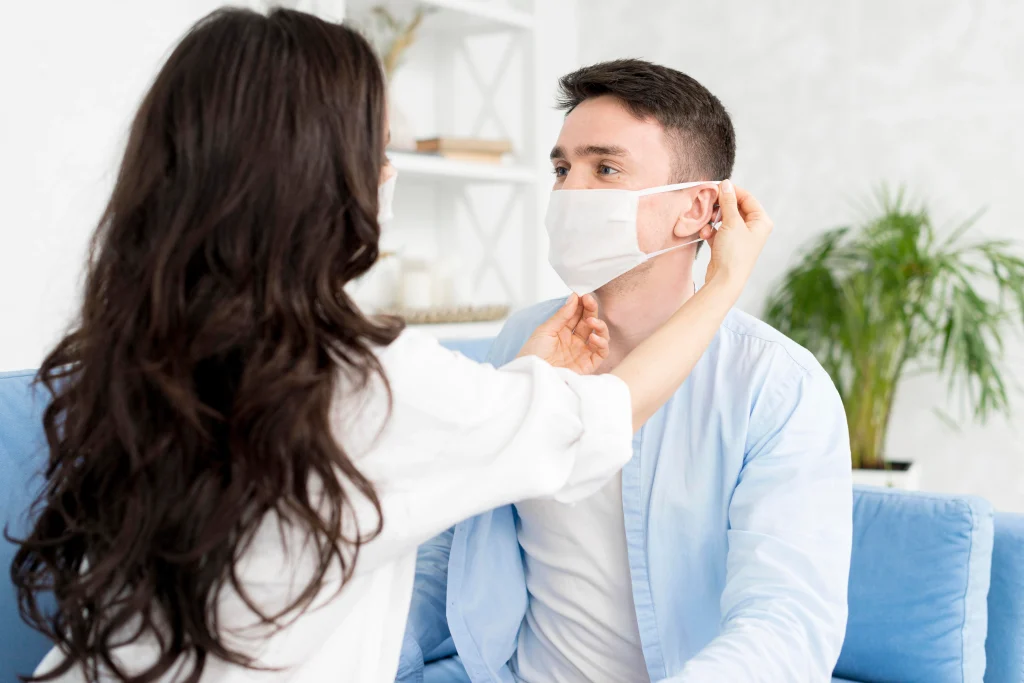 Woman helps a man adjust his face mask to prevent nasal polyps symptoms.