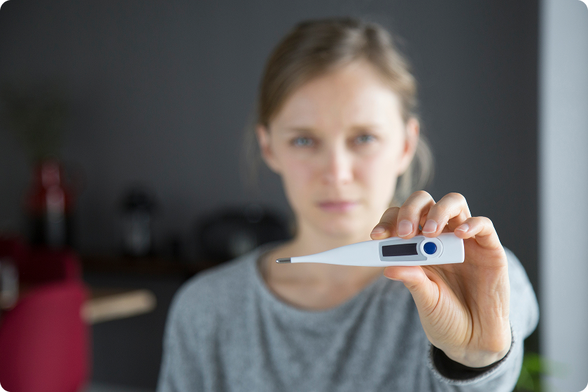 Woman holds a digital thermometer to check room temperature in Celsius indoors.