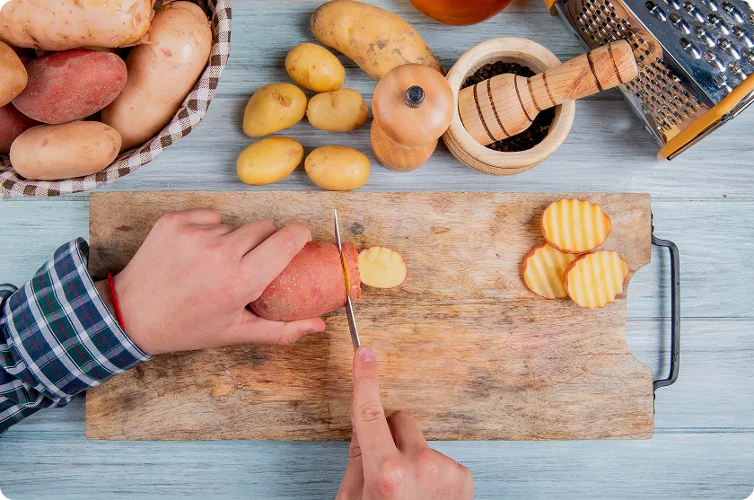 Hands slicing fresh red-skinned potatoes on a wooden board for sweet potato gerd digestion.
