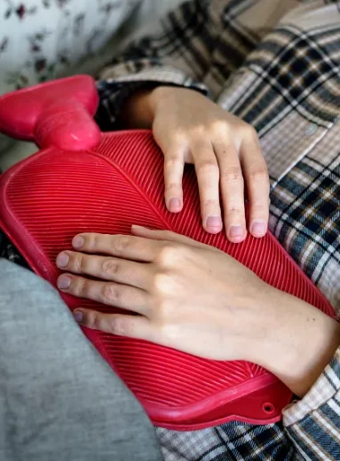Person applying a red heating pad for constipation to ease stomach pain