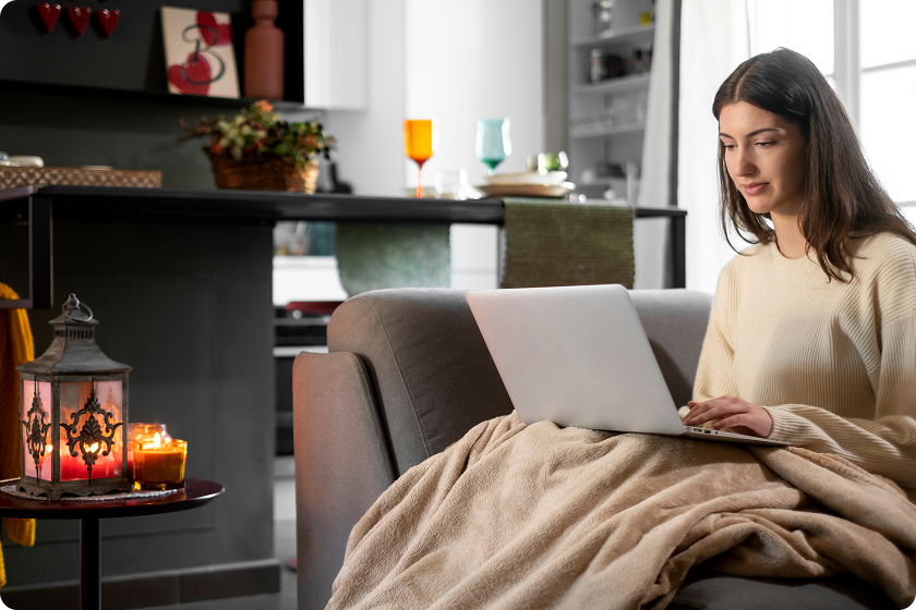 Woman works on laptop under a blanket at comfortable room temperature indoors.