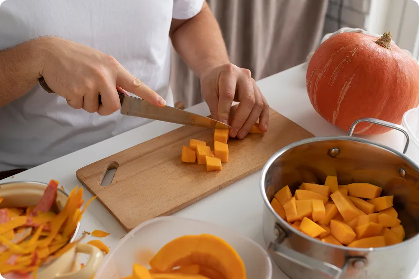 Slicing fresh orange vegetables on a wooden cutting board to prepare GERD friendly foods.