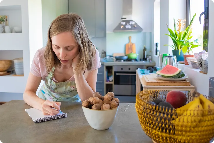 Woman writing meal plan notes near healthy whole foods including sweet potato for acid reflux.