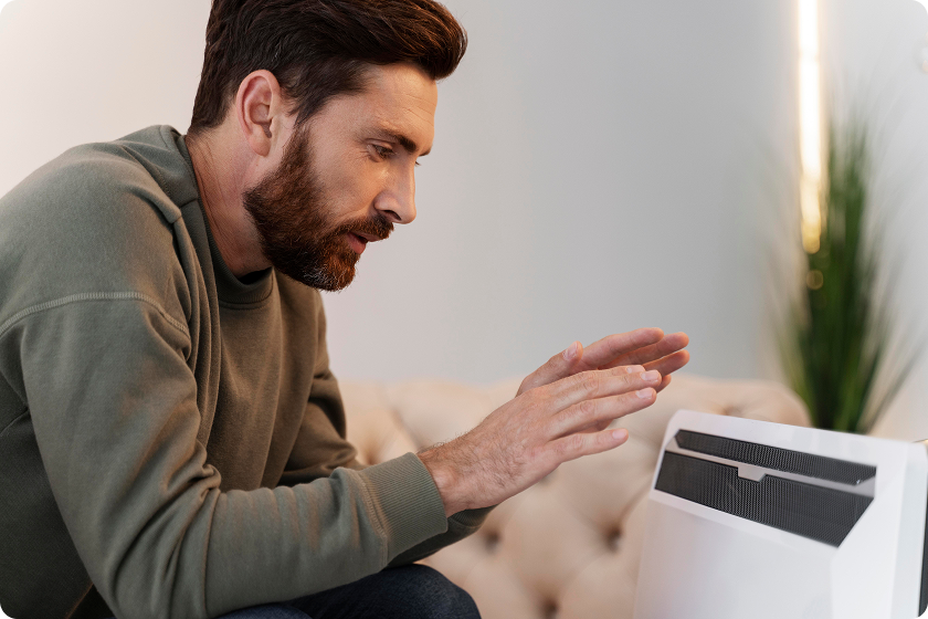 Man warms hands near space heater to reach ideal indoor temperature comfortably.
