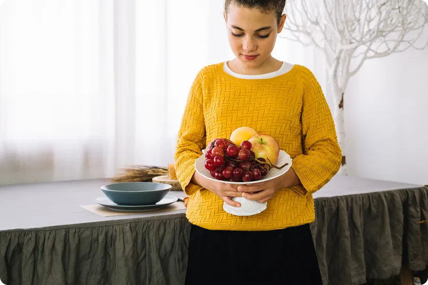 Person holding fresh fruit pedestal bowl featuring sweet potatoes acid reflux dietary options.